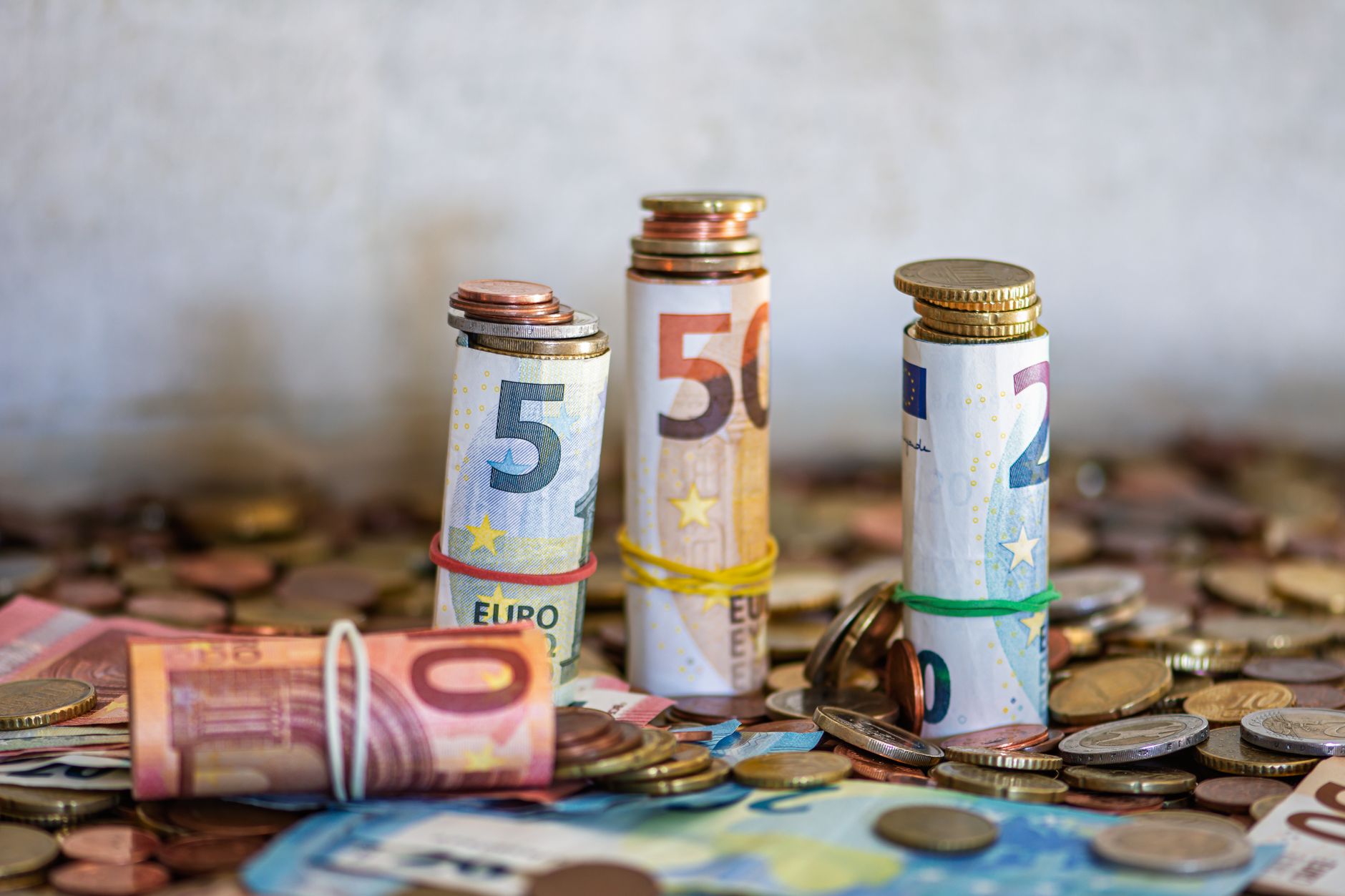 Billets en euros roulés avec des élastiques et pièces de monnaie empilées.