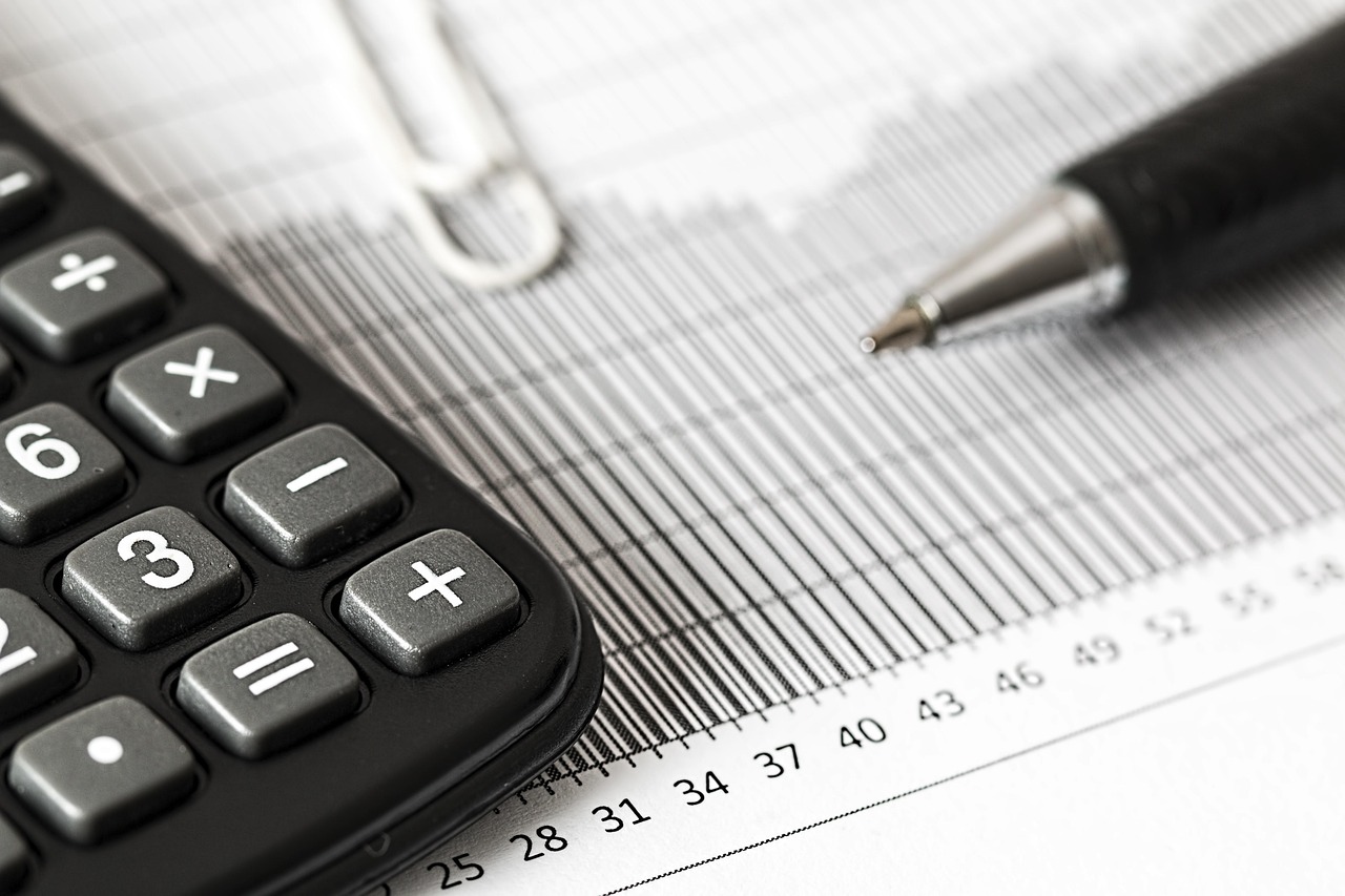 Gros plan sur une calculatrice, un stylo et un trombone posés sur un document couvert de chiffres