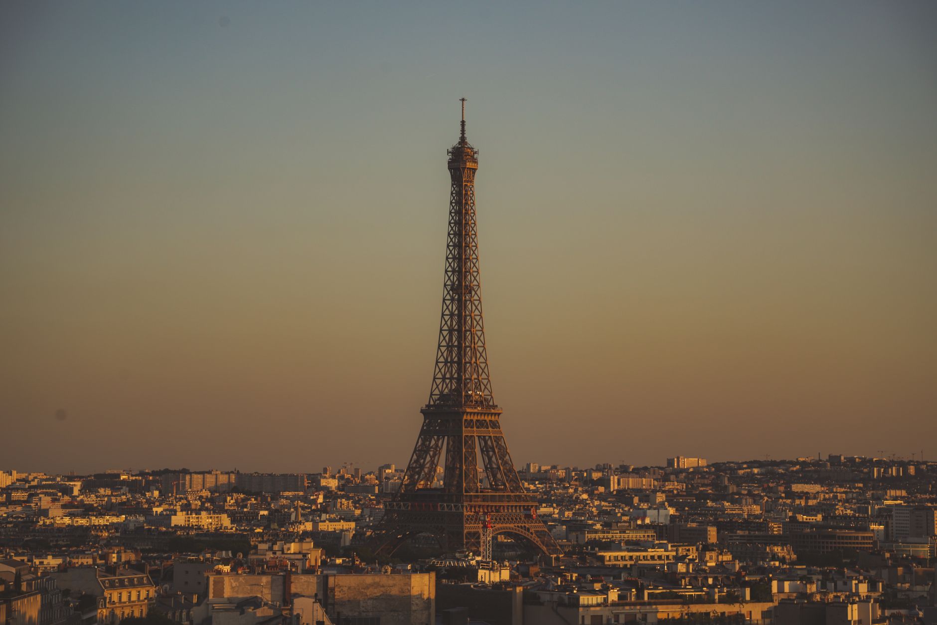 La Tour Eiffel se détache au coucher du soleil au-dessus des toits d’une ville dense.